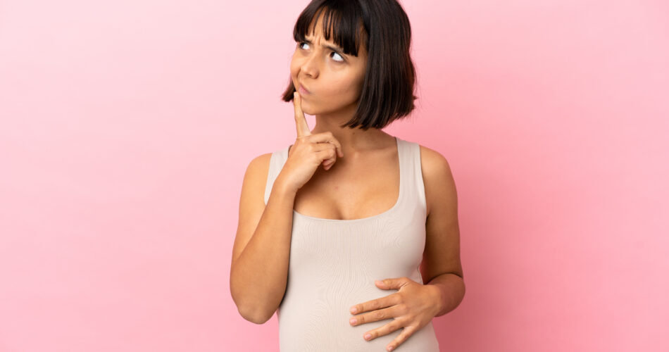Young pregnant woman over isolated pink background having doubts while looking up