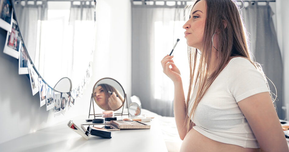pregnant woman applies makeup home front mirror